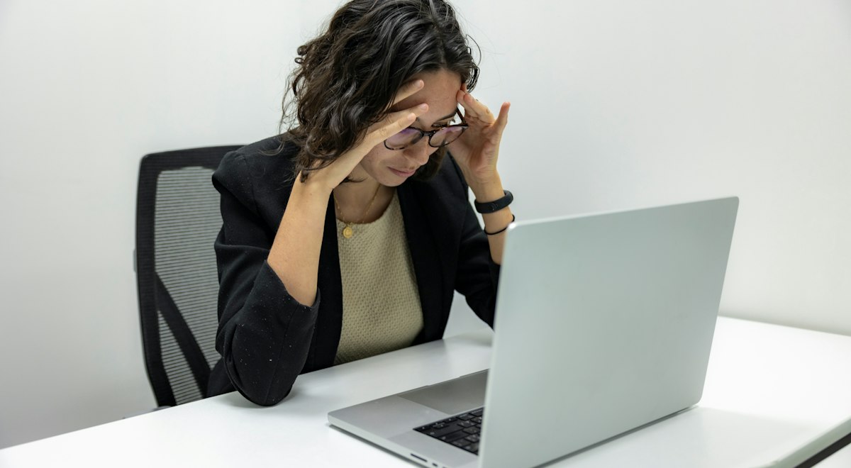 Woman rubbing her forehead in front of a laptop showing computer vision syndrome fatigue